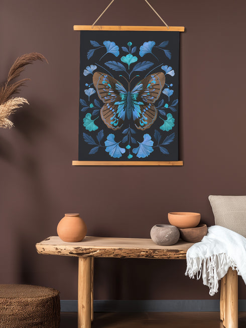 Wall hanging tapestry featuring a large copper butterfly with turquoise and azure blue markings surrounded by blue ginkgo leaves on black background. The textile hangs from wooden dowels with twine, showing detailed 3D embroidery-like texture.